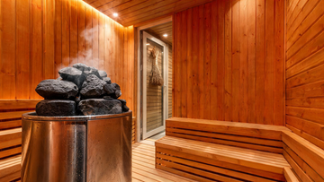 A large luxury sauna interior viewed at a wide three-quarter angle — thick Grade-A western red cedar tongue-and-groove walls…