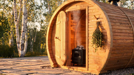 A wide three-quarter view of a Grade-A Canadian cedar barrel sauna on a landscaped outdoor deck, round door slightly open to…