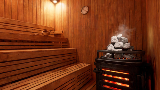 Interior of a traditional Finnish-style cedar sauna with warm amber lighting, a Harvia-style kiuas heater glowing in the…