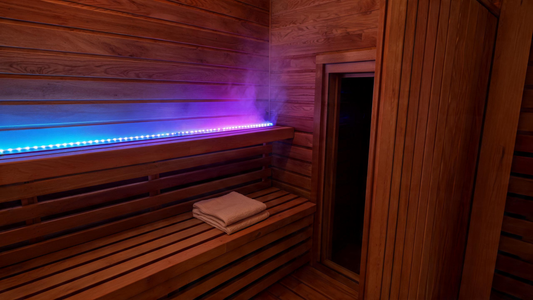 The interior of a cedar infrared sauna cabin bathed in a soft blue-to-purple gradient from LED strips mounted along the…