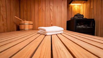 Interior of a Grade-A Canadian cedar sauna, wide bench viewed at low angle with a neatly folded white towel resting on the…