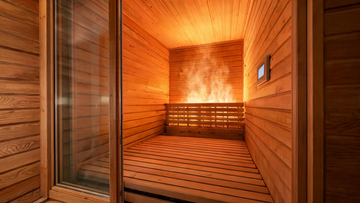 A premium cedar infrared sauna cabin photographed at a low three-quarter angle, interior panels glowing warm amber from…