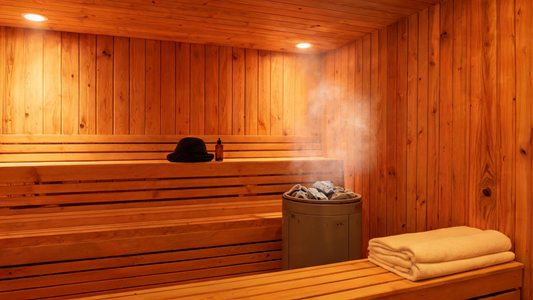 Interior of a Grade-A Canadian cedar sauna, warm amber glow from overhead lighting, a neatly folded wool sauna hat resting…