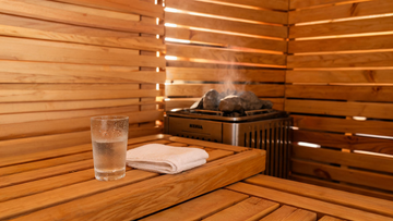 Interior of a Canadian hemlock sauna with warm amber light filtering through cedar slats, a glass of water with condensation…