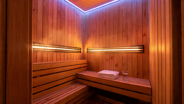 A cedar-panelled infrared sauna interior glowing with warm amber light from carbon heater panels along both walls, a neatly…