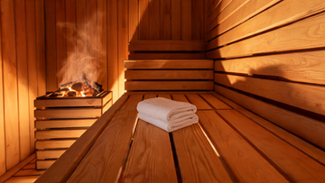 The interior of a warm cedar sauna cabin viewed from bench level, a neatly folded white cotton towel resting on the lower…