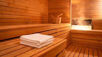 Interior of a warm cedar Finnish sauna, soft amber light on Grade-A Canadian cedar walls, a folded white towel resting on…