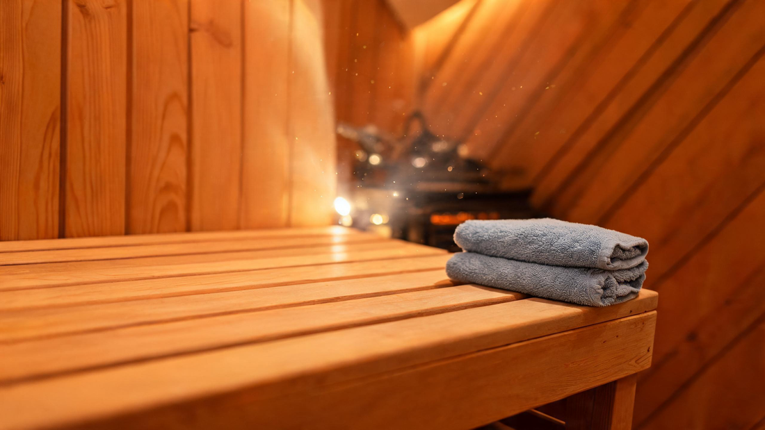 Close-up three-quarter angle of a sauna interior corner where cedar wall cladding meets a clear-grade bench, warm amber…