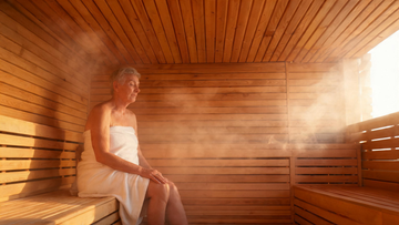 9) — warm cedar sauna interior, soft amber glow, a mature adult sitting calmly with hands resting on a knee, steam rising,…