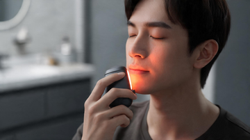 9) — A calm, premium home-wellness close-up: a person holding a small handheld red-light device near the lip area, warm…