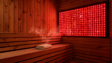 9, 1200x675) — HERO. Warm cedar infrared sauna interior with a wall of red and near-infrared LED panels glowing softly…