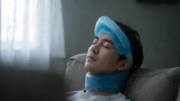 Editorial, calm image of a person resting in a dim room with a cool-toned gel wrap across the forehead and back of the neck, soft window light, hint