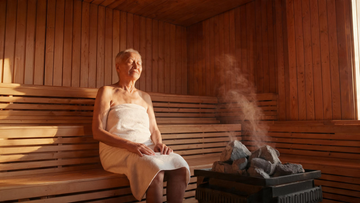 Also the OG/Twitter share image. Warm cedar sauna interior, an older adult sitting calmly on the bench in soft golden light, steam rising, serene and