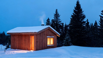 A Western Red Cedar outdoor sauna cabin in a snowy Canadian backyard at dusk, warm light glowing from the window, cedar grain visible on the exterior