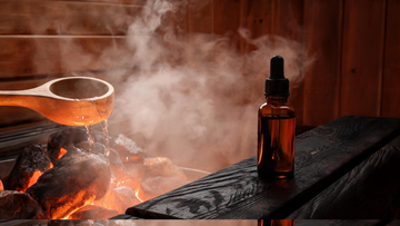 9) — Steam rising off dark cedar sauna rocks as a wooden ladle pours scented water; warm amber light, a small amber glass…