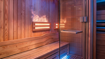 A full-spectrum infrared sauna interior shot at a low three-quarter angle — Grade-A Canadian cedar tongue-and-groove walls glowing amber under warm