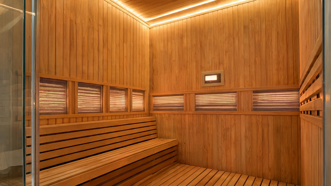 A warm, low-lit infrared sauna interior with Canadian hemlock panels, a single wide bench at a comfortable height, a precision digital control panel