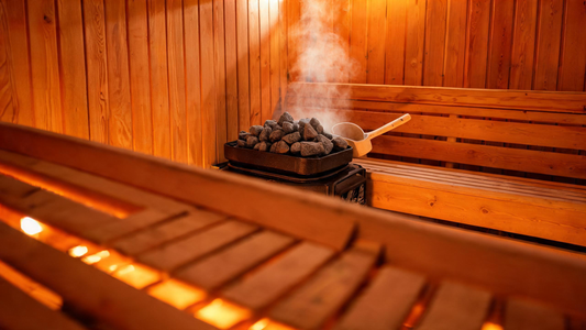 Interior of a warm cedar traditional sauna, soft golden light filtering through slatted benches, gentle wisps of steam rising from the heater stones, a