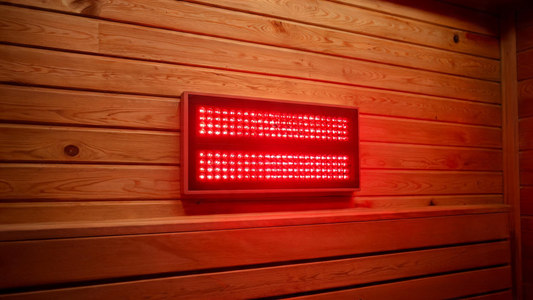 A Calore red-light therapy panel mounted on a cedar sauna wall, deep red and near-infrared LEDs glowing warmly across the panel face, warm cedar interior,