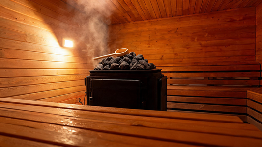 Interior of a cedar Finnish sauna, soft amber light on Grade-A Canadian cedar walls, a ladle resting on a Harvia heater piled with dark volcanic rocks, a