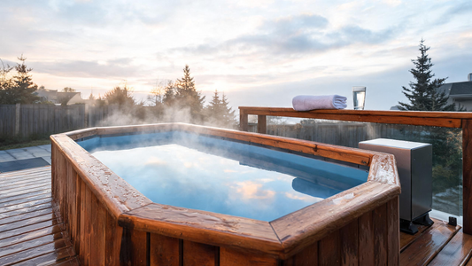 A sleek cedar-trimmed cold plunge tub on a misty Canadian deck at dawn, Glacier-blue still water reflecting early morning light, a folded towel and a