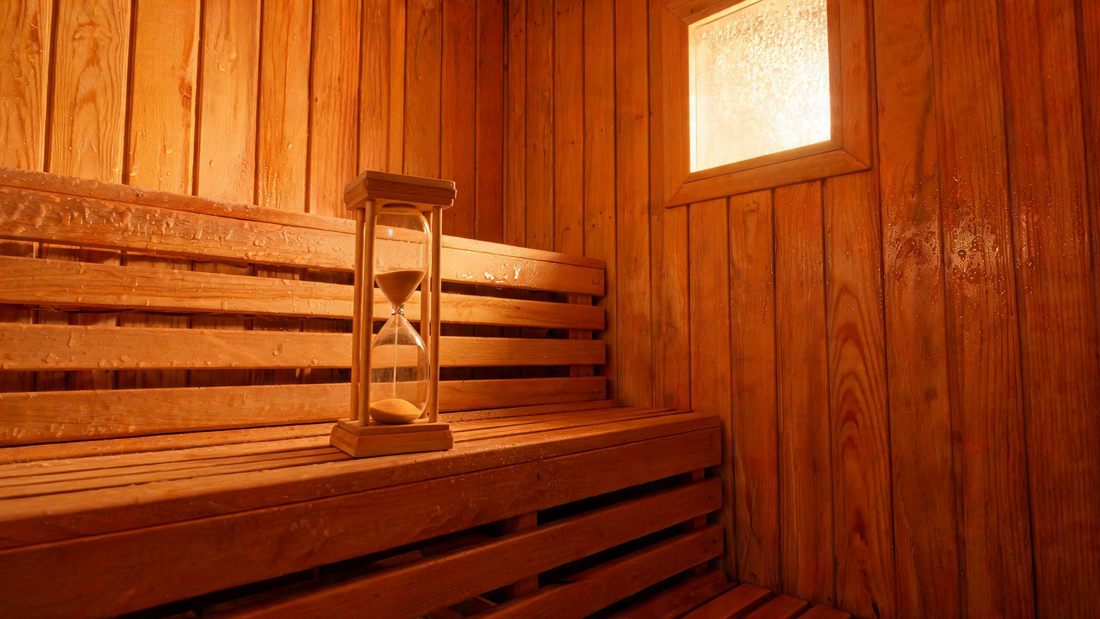 A warm cedar-panelled sauna interior viewed from a low angle, upper bench empty, a wooden hourglass timer on the bench rail with sand almost run through,