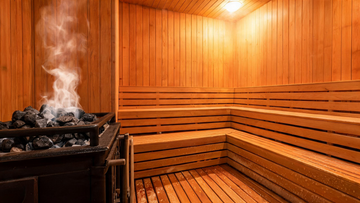 A serene traditional Finnish sauna interior, Grade-A Canadian cedar benches glowing in warm amber heat-lamp light, a Harvia stone heater with smooth grey