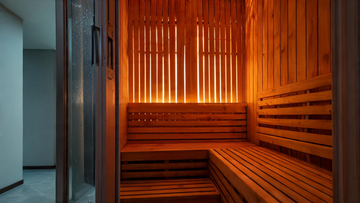 A warm cedar infrared sauna interior photographed through its glass door, soft amber light glowing through the wood slats, a clean bench and back panel