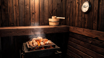 Interior of a Canadian black cedar traditional sauna, walls glowing warm amber from a low-mounted sauna heater with stacked…