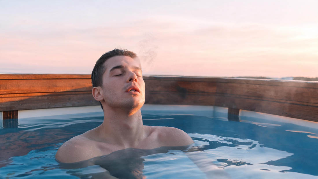 A calm person submerged to the shoulders in a sleek cold plunge at dawn, eyes closed, shoulders visibly softened (not braced), faint vapour