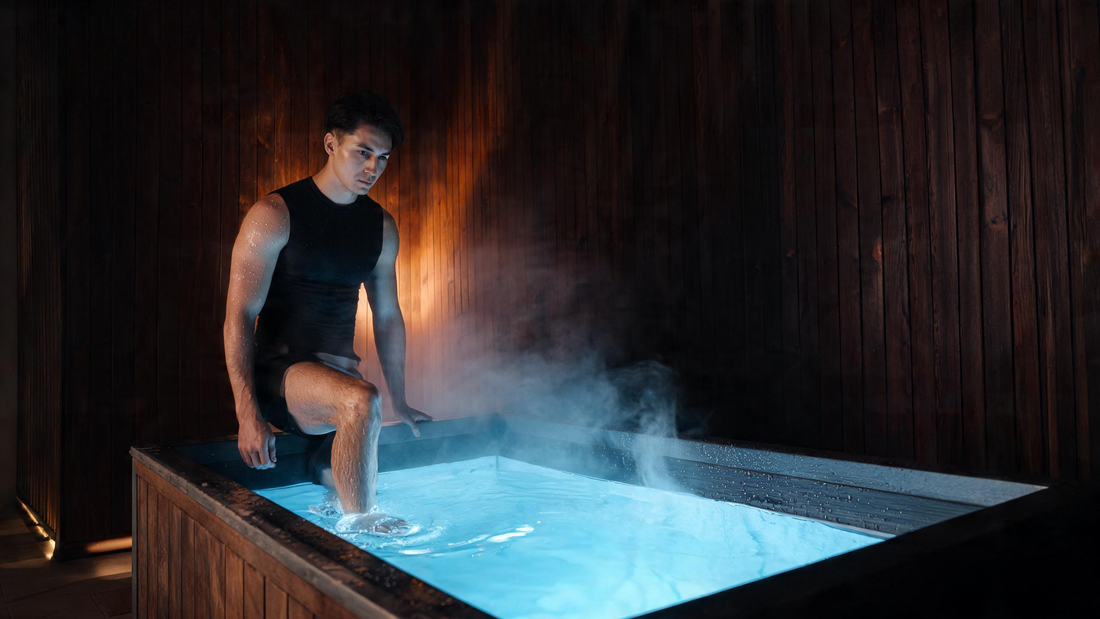 A calm, fit person stepping into a premium home cold plunge in a dark cedar wellness room, cold vapour drifting off Glacier-blue water